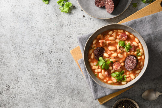 Asturiana traditional fabada with haricot, blood sausage served fresh crispy toast on gray stone table. View from above. Copy space. Spanish cuisine.