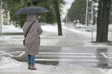 A girl in a winter jacket with an umbrella stands in front of the crossing.