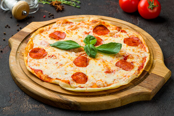 Pepperoni pizza with basil on wooden board on dark concrete table