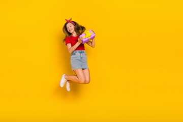 Fototapeta na wymiar Full body photo of cute teenager girl jump hold present wear t-shirt hairband skirt footwear isolated on yellow background