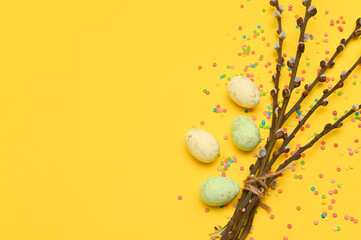 Willow branches with buds on a yellow background. Easter eggs are lying nearby. Copy space