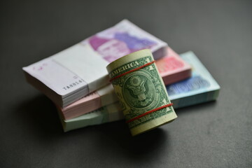 A roll of US Dollar bills over  Pak Rupee cash stacks of different denominations. Currency war concept, Falling Rupee value in Pakistan against US Dollar. Shallow depth of field. Selective focus.