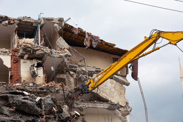 A yellow excavator is working on demolishing an old house in the city of Alanya, Turkey
