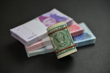 A roll of US Dollar bills over  Pak Rupee cash stacks of different denominations. Currency war concept, Falling Rupee value in Pakistan against US Dollar. Shallow depth of field. Selective focus.