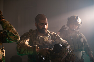 Bearded man in military equipment in dark room. Men in uniforms holding machine gun, getting ready...