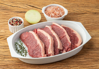 Sliced raw strip loin meat over white plate with seasonings