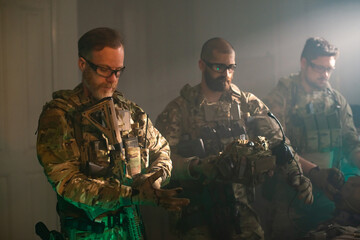 Bearded men in military equipment in dark room. Men in uniforms holding machine gun, getting ready...