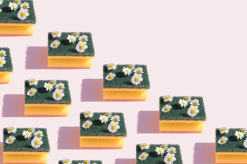 Dishwashing sponge with daisy spring flowers arranged in a pattern on a pink background. Surreal grass and flower concept.