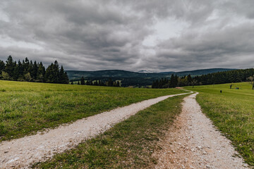 Fototapeta na wymiar A wide dirt road winding through rural landscape. Rolling hills, green grass and cloudy sky.