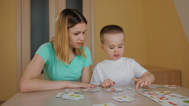 Cute pretty child learning and studying with his young mother. Little boy spend time playing educational card game with tutor mom at home. Enjoying maternity, childhood recreation