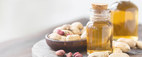 Obraz na płótnie Canvas Concept of organic vegetable oils for cooking and cosmetology. Peanut nuts to illustrate ingredients. Rustic wooden background, pure natural oil in glass bottles. Close up, banner, copy space