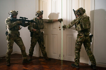 Focused bearded men in military equipment standing near door. Men in uniforms holding machine gun,...