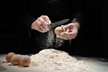 woman breaks the egg into flour to knead the dough on black background. 