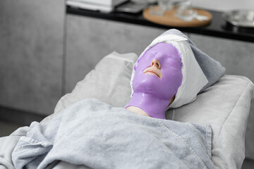Young beautiful woman doing beauty treatment, purple mask with blueberry in the salon.