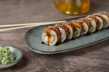 Sushi rolls on a gray oblong plate. Served with a kettle of tea and soy sauce