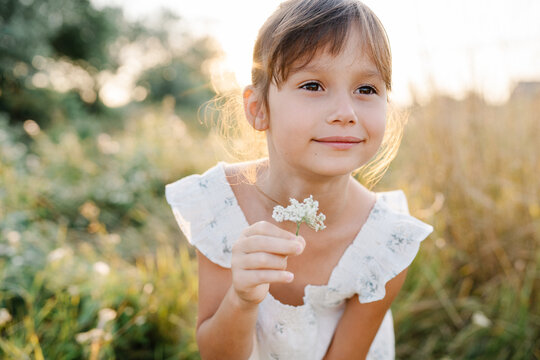Adorable little girl wearing natural white dress with wildflower motiv in green field with wild carrot flowers at summer, outdoor lifestyle. Freedom concept