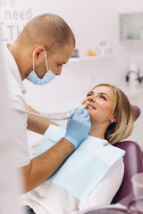 A dentist in a mask and goggles treats a woman's teeth.