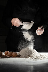 woman sifts flour through sieve onto table with eggs on black background. 