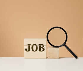 Wooden cubes with the inscription work and a black magnifier on a white table. Job search, unemployment