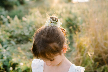 Tender little girl wearing natural white dress with wildflower motiv with wild carrot flowers in hair standing in the field at summer, outdoor lifestyle backlit photo.