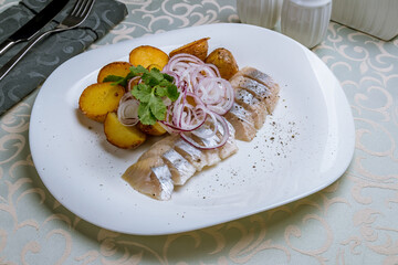 Herring with potatoes and red onion on a white plate