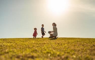 Parent child relationship concept. Mother playing with her children outdoors in a grass field 