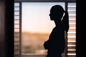 Woman in a dark room looking out window early morning 