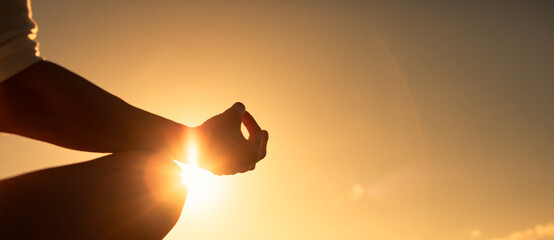 Hand meditating against sunset sky background. Peace and calm in nature 