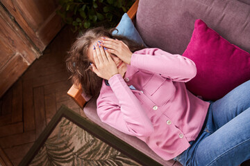 Depressed girl closed her face with her hands and crying while lying on couch