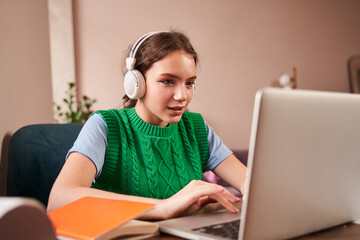 Teen wearing headphones typing at the laptop computer while doing her homework