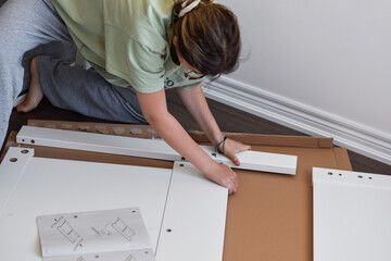 Young girl assembling new furniture using instruction manual