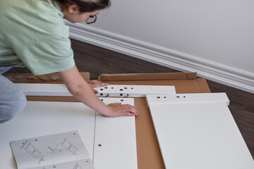 Young girl assembling new furniture using instruction manual