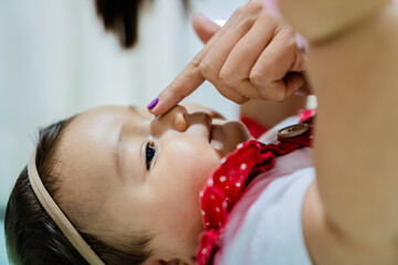 baby latina girl lying on the floor, mother puts finger on her nose