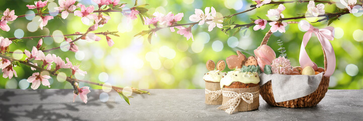 Easter basket with painted eggs, cakes and blooming branches outdoors