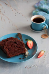Chocolate cake placed on a blue plate with a blue cup of coffee, decorated with strawberries