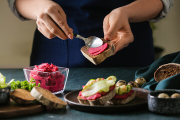 Woman making tasty sandwich with healthy hummus at table