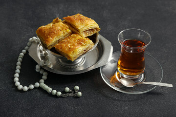 Tasty Turkish baklava with tasbih and tea on dark background