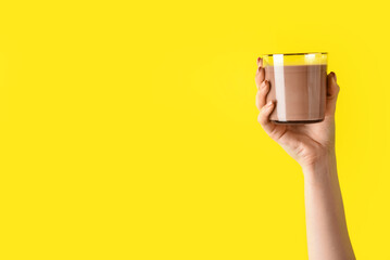 Female hand holding glass of delicious chocolate milk on color background