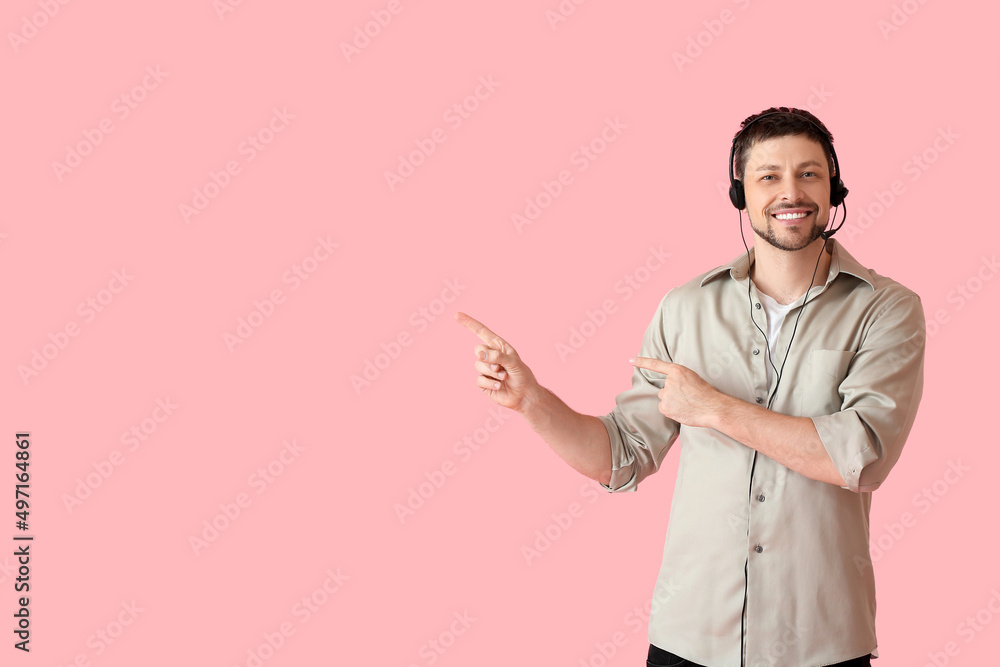 Poster smiling consultant of call center in headset pointing at something on pink background