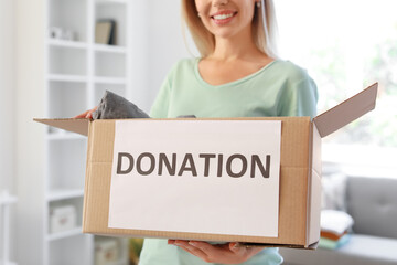 Young woman holding box with donation clothes at home