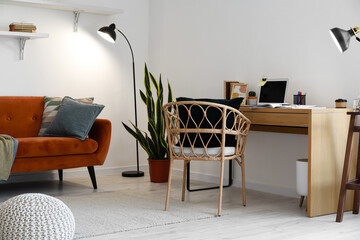 Modern workplace with laptop, wicker chair and red sofa in living room