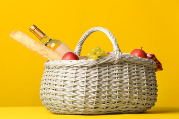 Wicker basket with tasty food and wine for picnic on color background