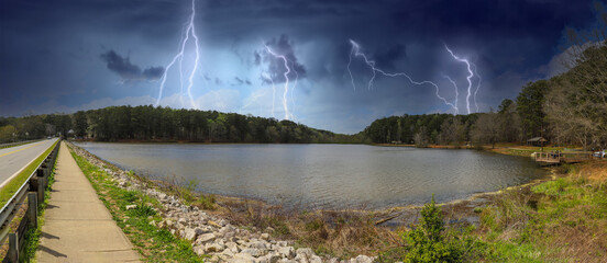 a panoramic shot of a vast rippling lake surrounded by lush green trees with powerful storm clouds...
