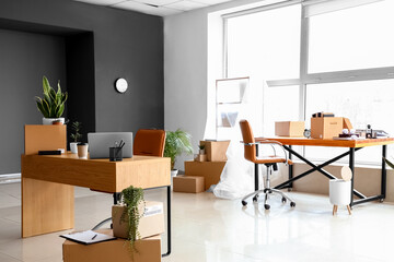 Cardboard boxes with belongings and furniture in interior of office on moving day