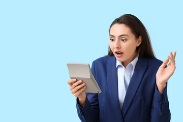 Shocked young businesswoman with calculator on blue background