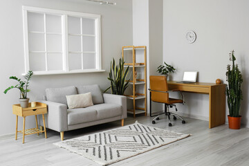 Interior of light living room with grey sofa and modern workplace