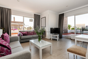 Living room of a penthouse apartment with two large terraces, gray fabric sofas and white wooden furniture and purple cushions