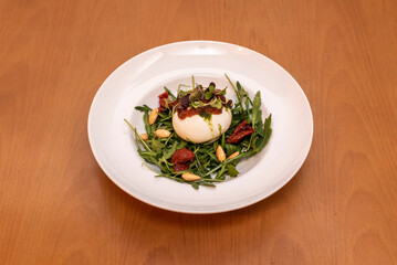 Typical Italian burrata salad with arugula, dehydrated tomato with olive oil, pesto sauce and fried peeled almonds