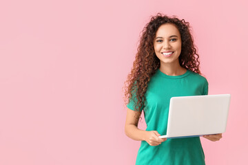 Young African-American woman with laptop on pink background