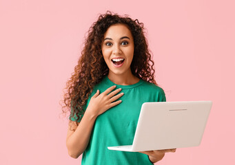Surprised young African-American woman with laptop on pink background